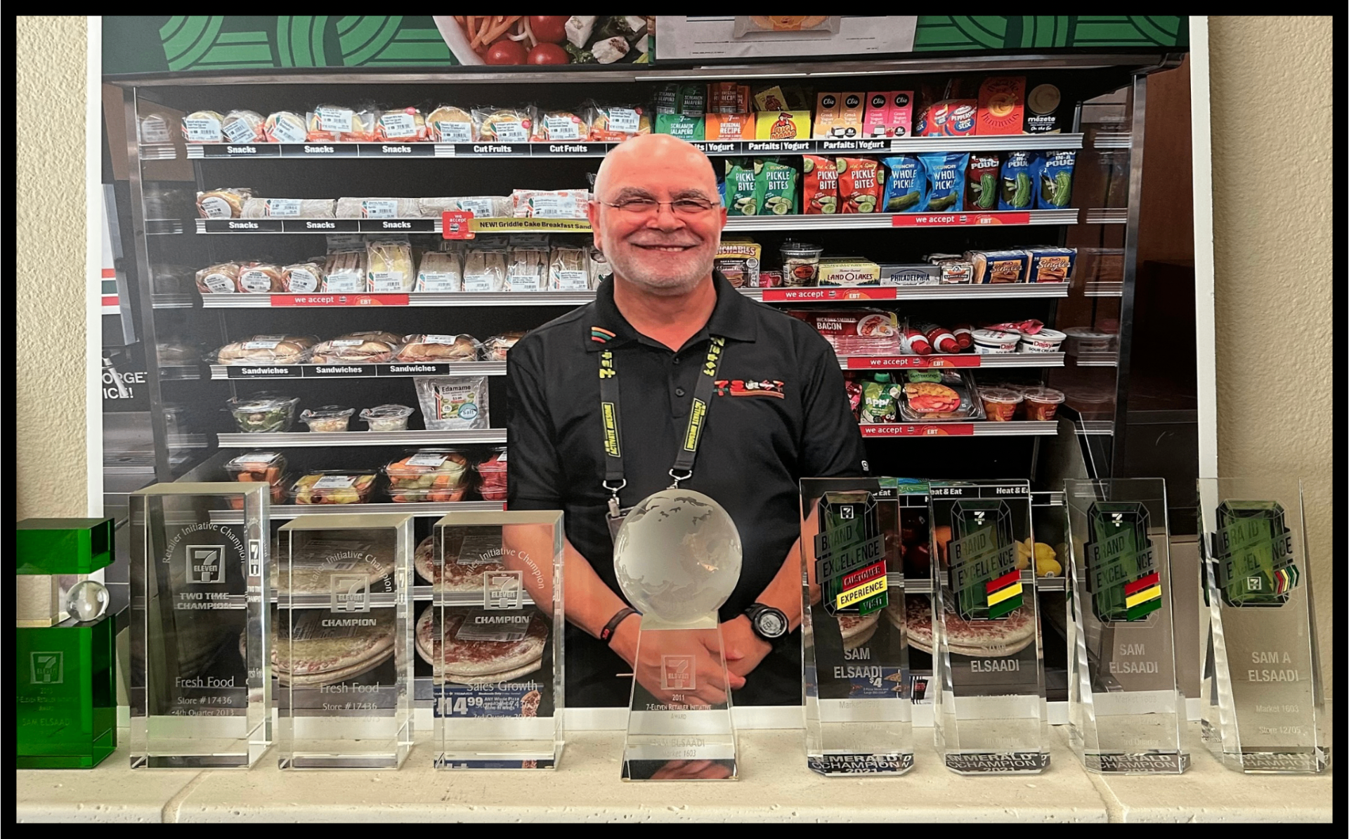 Sam Elsaadi standing behind a row of 7-Eleven crystal trophies.